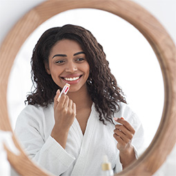 Woman looking in a mirror putting on Blistex Lip Balm